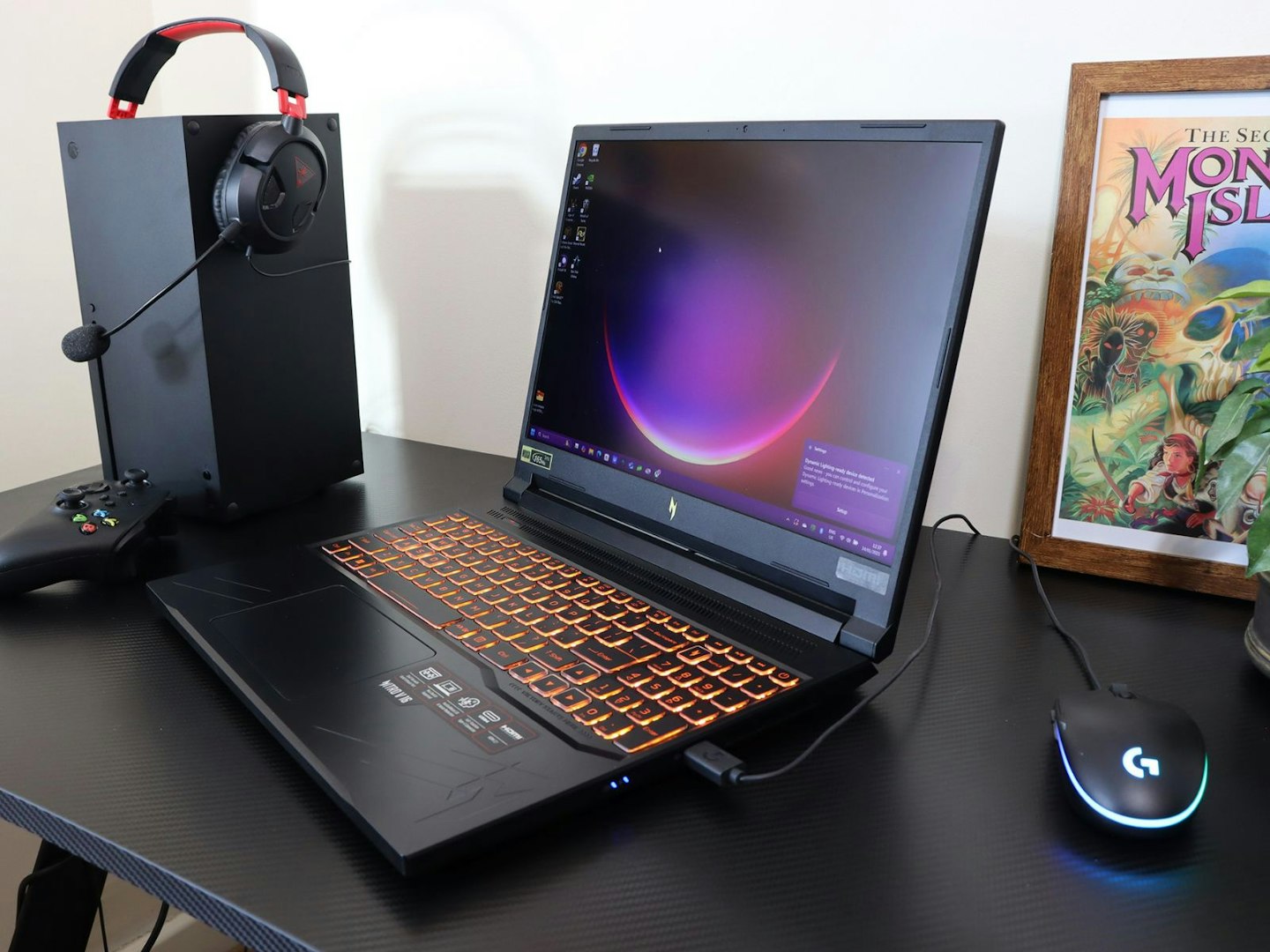 An Acer Nitro V 16 gaming laptop on a desk with an xbox one, controller and headset