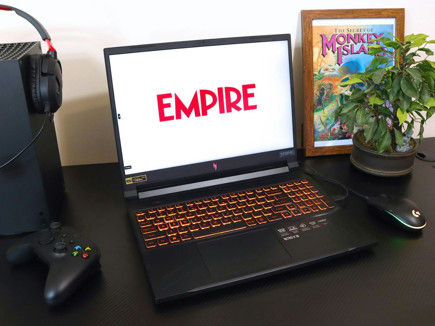 A gaming desk with laptop showing the Empire logo, a controller and headset