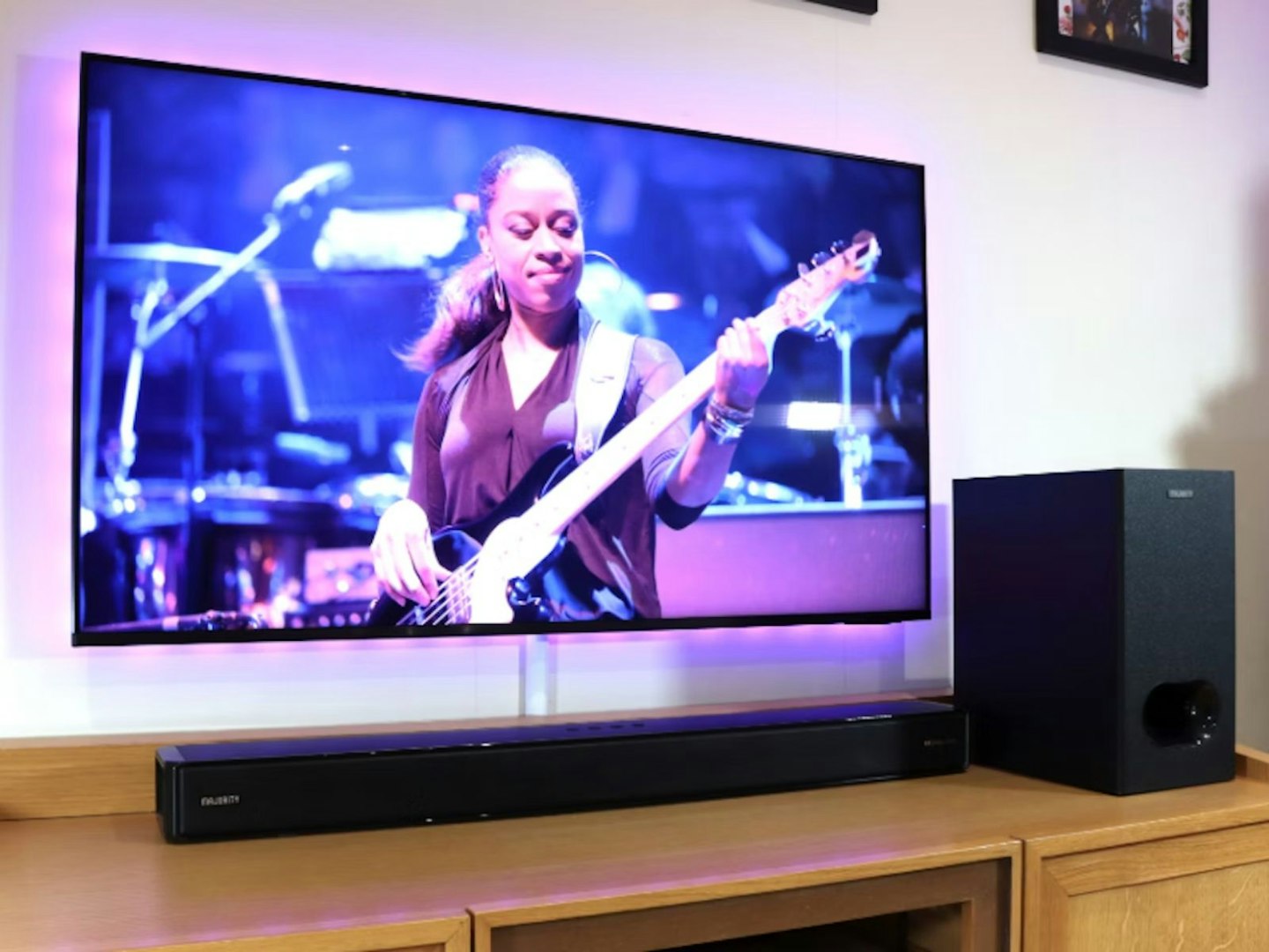 A soundbar and subwoofer next to a TV showing a guitar player